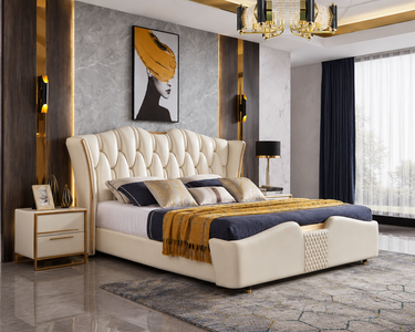 A luxury upholstered bed with a high tufted cream headboard and matching footboard, styled in a modern bedroom with gold and gray accents, navy blue bedding, and a gold throw blanket.