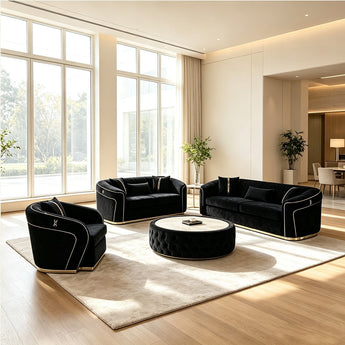 A luxury living room furniture set featuring a black velvet loveseat, a matching armchair, a three-seat sofa, and a round tufted coffee table, all arranged on a beige area rug in a modern, sunlit room with large windows.