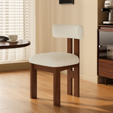Wooden chair with white cushioned seat and backrest in a room with a window and desk.