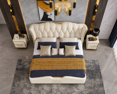 A luxury cream tufted leather bed with navy and gold bedding, styled in a modern, high-end bedroom setting with a geometric rug, gold side tables, and a chandelier.
